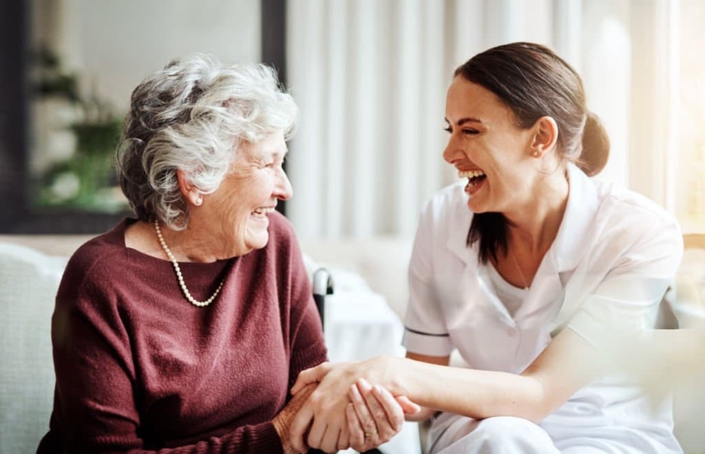A nurse laughing with an older patient, holding her hand