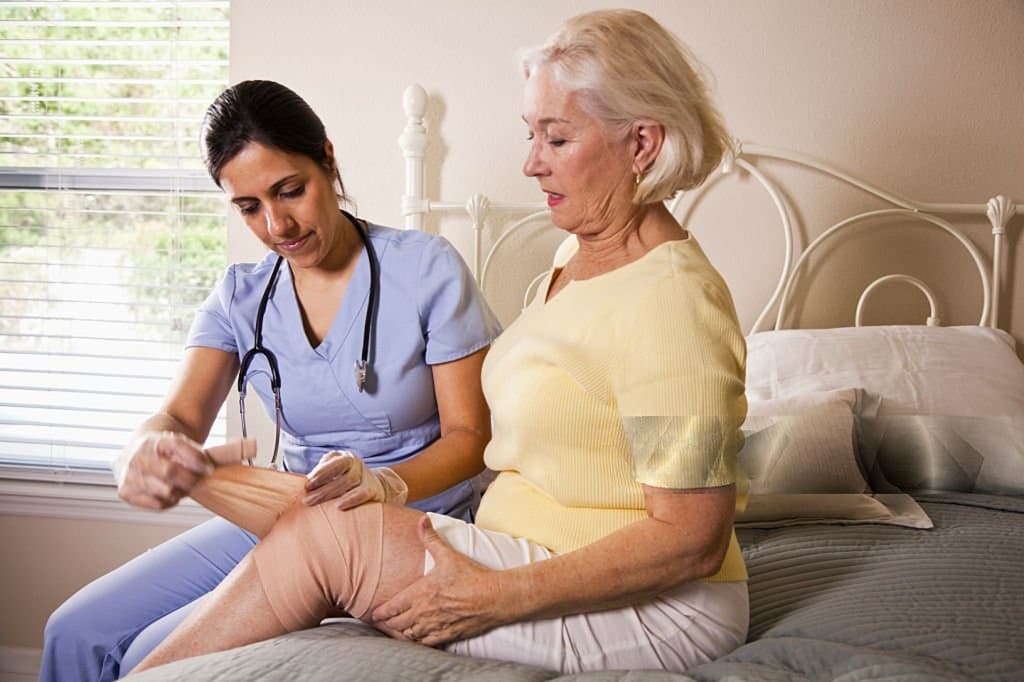 A nurse wrapping a patient's knee at her bedside at home