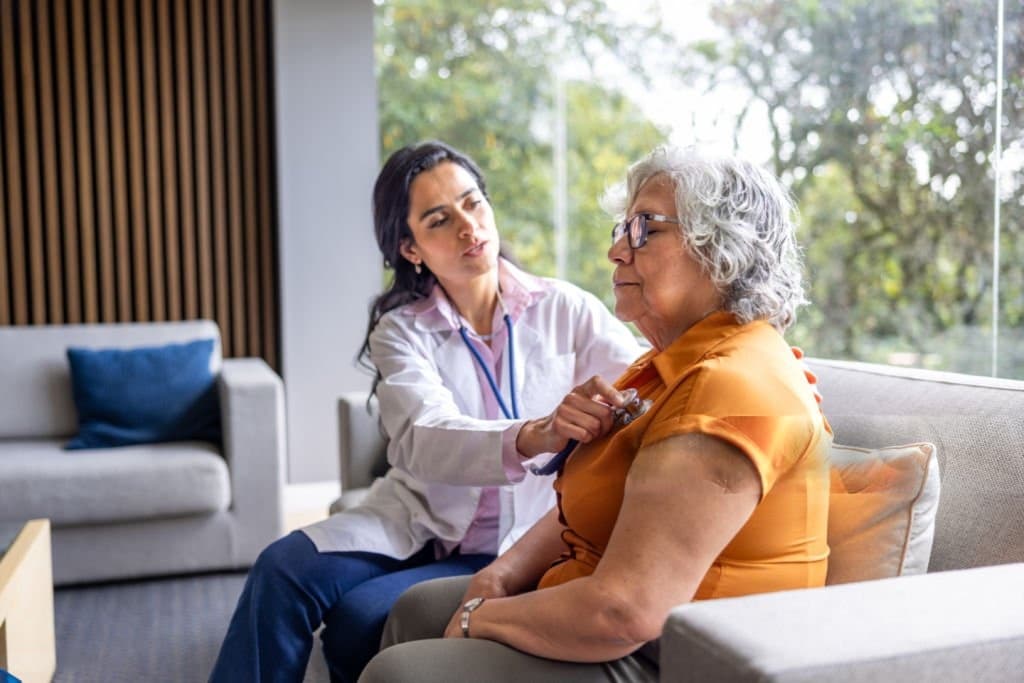 A nurse listening to an older patient's heart with a stethoscope at home
