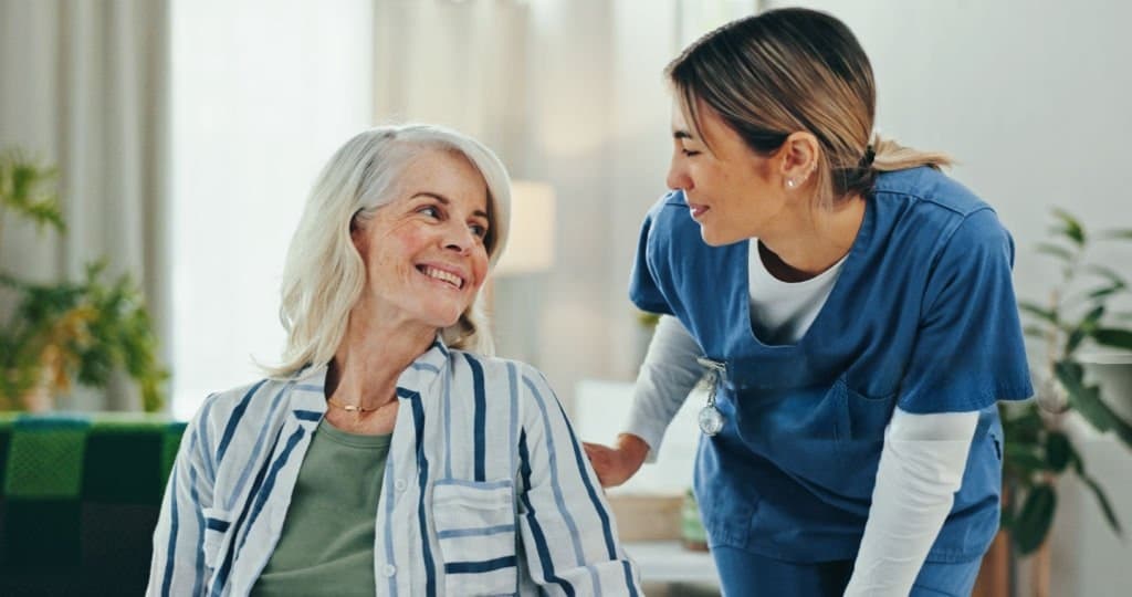A nurse leaning in to talk with a smiling older patient at home