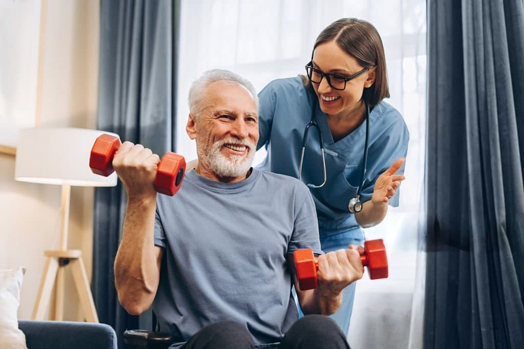 A nurse encouraging an older patient through light dumbbell exercises at home